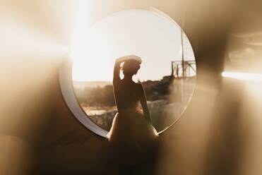 Rückenansicht Silhouette von anonymen anmutige Dame in Tanzkostüm stehend in der Nähe von runden Loch gegen unscharfen Natur Hintergrund und Blick weg - ADSF13252