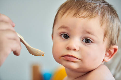 Nahaufnahme eines niedlichen kleinen Babys, das Püree von einem Löffel isst, der von einer anonymen Mutter gehalten wird - ADSF13359