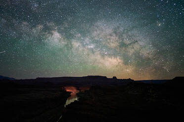 Spectacular view of luminous starry sky with Milky way reflecting in river flowing among dark rocky terrain in night time in USA - ADSF13373
