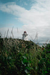 Famous Peggys Cove Lighthouse located on green cliff against cloudy sky on seashore in Canada - ADSF13406