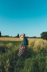 Rückenansicht einer unkenntlichen Bäuerin mit Hut, die an einem sonnigen Nachmittag ihre Weizenernte betrachtet - ADSF13425