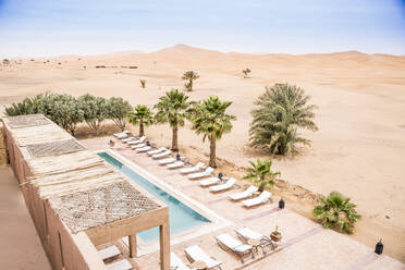 From above of stone terrace with pool and sunbeds among rare palms in desert sand, Morocco - ADSF13450