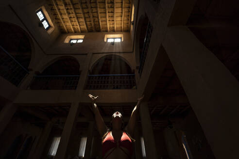 Von unten: Eine Frau erhebt die Hände und betet unter den Sonnenstrahlen in einer dunklen Kirche in Marokko - ADSF13461