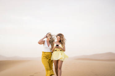 Fröhlich stilvolle zwei blonde Frauen Freunde mit Handy beim Wandern in der Wüste von Marokko - ADSF13471