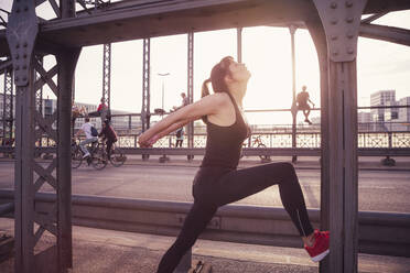 Frau beim Sport auf einer Brücke in der Stadt bei Sonnenuntergang - DHEF00319