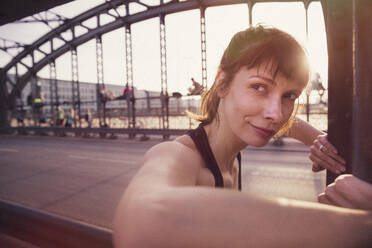 Schöne Frau schaut weg, während sie auf einer Brücke bei Sonnenuntergang trainiert - DHEF00320