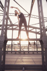 Woman exercising on metal bridge at sunset - DHEF00325