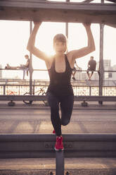 Beautiful woman stretching railing at bridge during sunset - DHEF00334