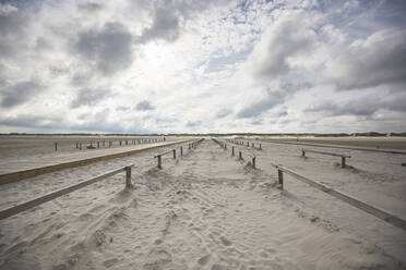 Wolken über hölzernen Geländern, die sich entlang des breiten Sandstrandes erstrecken - ASCF01413