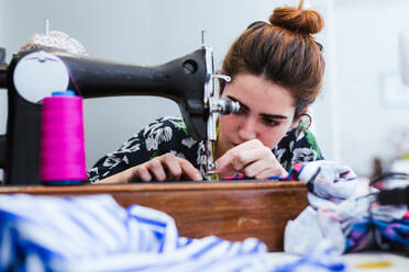 Teenage girl student practicing sewing on modern machine in cozy workshop - ADSF13488