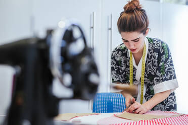 Teenage girl student practicing sewing on modern machine in cozy workshop - ADSF13491