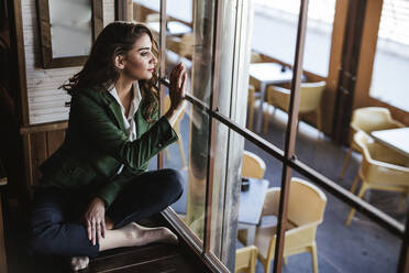 From above of pensive trendy woman sitting with crossed legs and looking through window of modern cafe - ADSF13498