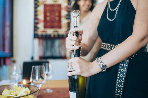 Frau öffnet Weinflasche während eines geselligen Beisammenseins zu Hause - MEUF01961