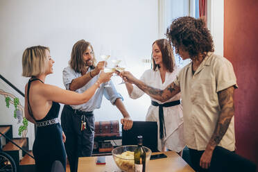 Männliche und weibliche Freunde stoßen mit Weingläsern während einer Party zu Hause an - MEUF01964