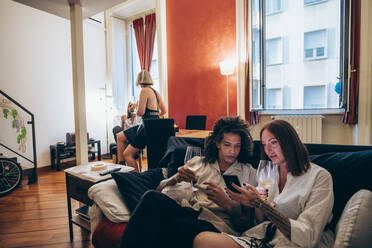 Frau zeigt einem männlichen Freund ihr Smartphone, während sie zu Hause auf dem Sofa Wein trinkt - MEUF01970