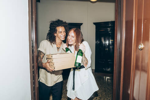 Fröhliche Freunde mit Bierflaschen und Pizzakartons am Eingang eines Hauses während einer Party - MEUF01978