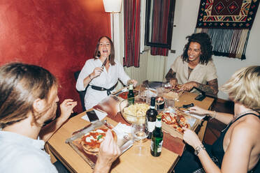 Happy male and female friends eating pizza during social gathering at home - MEUF01979