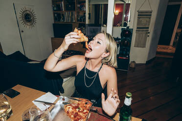 Junge Frau genießt Pizza während einer Party zu Hause - MEUF01984