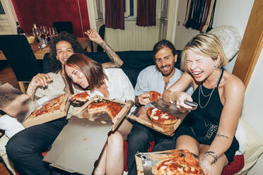 Fröhliche Freunde sehen fern, während sie auf einer Party zu Hause Pizza essen - MEUF01990