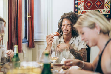 Glücklicher Mann beim Essen, während er mit Freunden zu Hause eine Party feiert - MEUF01993