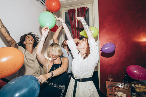 Male and female friends dancing with colorful balloons during party stock photo