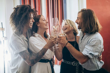 Fröhliche männliche und weibliche Freunde stoßen mit Weingläsern während einer Party zu Hause an - MEUF02013