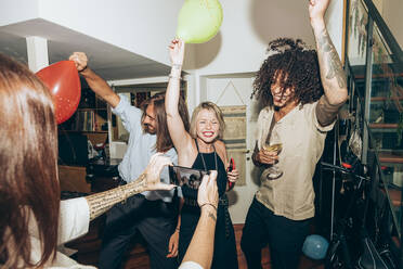 Woman photographing happy friends dancing during social gathering at home - MEUF02028