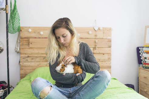 Frau hält Meerschweinchen im Arm, während sie zu Hause auf dem Bett sitzt - SKCF00681