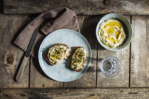 Ein Glas Wasser und Brotscheiben mit Hummus und Sprossen - EVGF03727