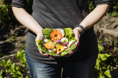 Close-up of woman holding plate with lettuce and edible flowers - EVGF03729
