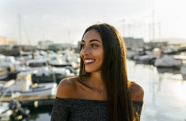 Beautiful woman smiling while standing at harbor during sunset - MGOF04375