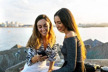 Freunde lächelnd bei der Benutzung eines Mobiltelefons an der Promenade - MGOF04391