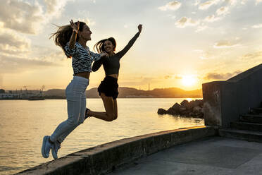 Young women enjoying while jumping at promenade during sunset - MGOF04395