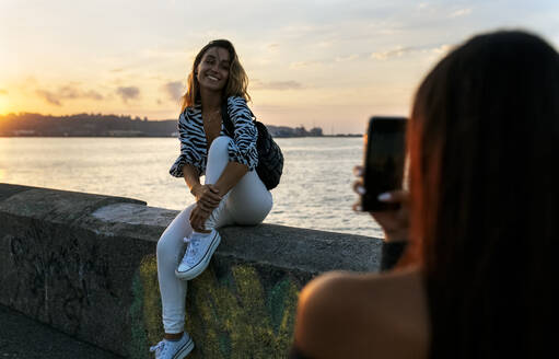 Ein Freund fotografiert eine Frau, die auf einer Stützmauer an der Promenade sitzt - MGOF04402