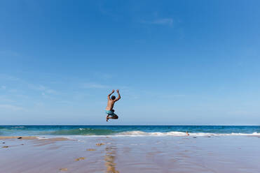 Back view of unrecognizable man in swimwear enjoying summer holidays and jumping into sea water against blue sky in sunny day - ADSF13632