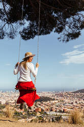 Girl having fun with red skirt and hat swinging while contemplating the city in the background - ADSF13674