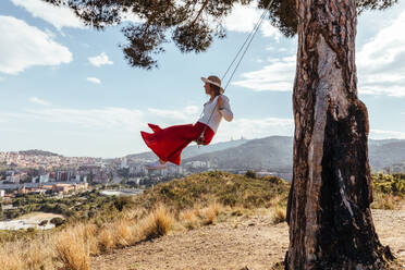 Girl having fun with red skirt and hat swinging while contemplating the city in the background - ADSF13675