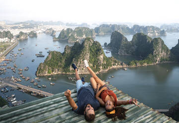 Von oben Blick auf das liebende Paar, das auf dem Metalldach liegt und die malerische Aussicht auf die Halong-Bucht in Vietnam betrachtet - ADSF13699