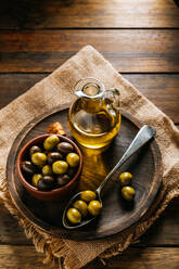 From above glass jar with extra virgin oil placed on wooden plate with black and green olives - ADSF13737