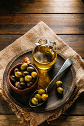 Von oben Glasgefäß mit nativem Olivenöl extra auf Holzteller mit schwarzen und grünen Oliven - ADSF13737