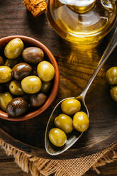 From above glass jar with extra virgin oil placed on wooden plate with black and green olives - ADSF13738