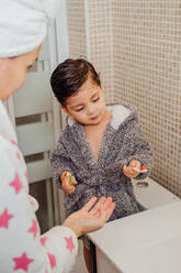 Niedlicher kleiner Junge im Bademantel und lächelnde Mutter mit Handtuch-Turban im Bad stehend und Zähne putzend - ADSF13762
