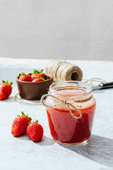 Composition with fresh homemade strawberry juice in glass jar wrapped with twine placed on marble surface with whole berries and knife - ADSF13774