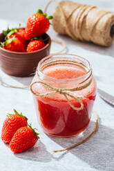 Composition with fresh homemade strawberry juice in glass jar wrapped with twine placed on marble surface with whole berries and knife - ADSF13777