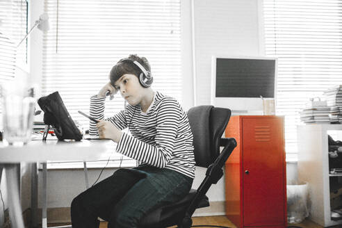 Boy doing home schooling on tablet computer sitting at desk - MMFF01292