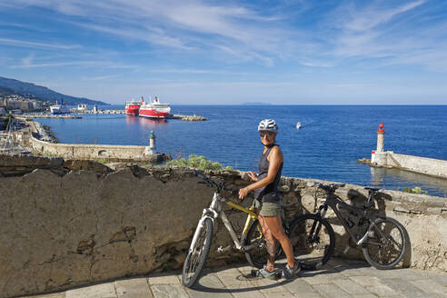 Frankreich, Haute-Corse, Bastia, Porträt einer erwachsenen Frau, die mit einem Fahrrad vor einer Küstenmauer posiert - UMF01004