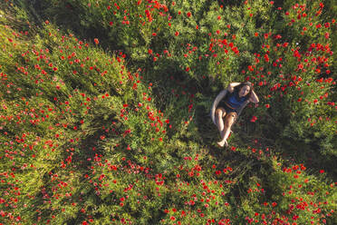 Young woman sitting in basket-chair on poppy field - ASCF01424