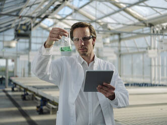 Scientist with tablet examining liquid in a greenhouse - JOSEF01583