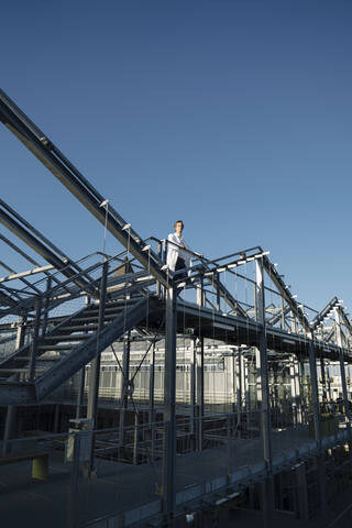 Wissenschaftlerin auf einer Metallkonstruktion unter blauem Himmel, lizenzfreies Stockfoto