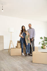 Happy family standing by cardboard boxes against wall in new home - MJFKF00549